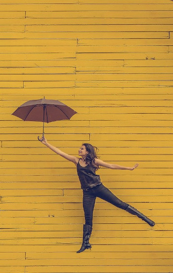 a young woman holding an umbrella and jumping up in front of a yellow wall